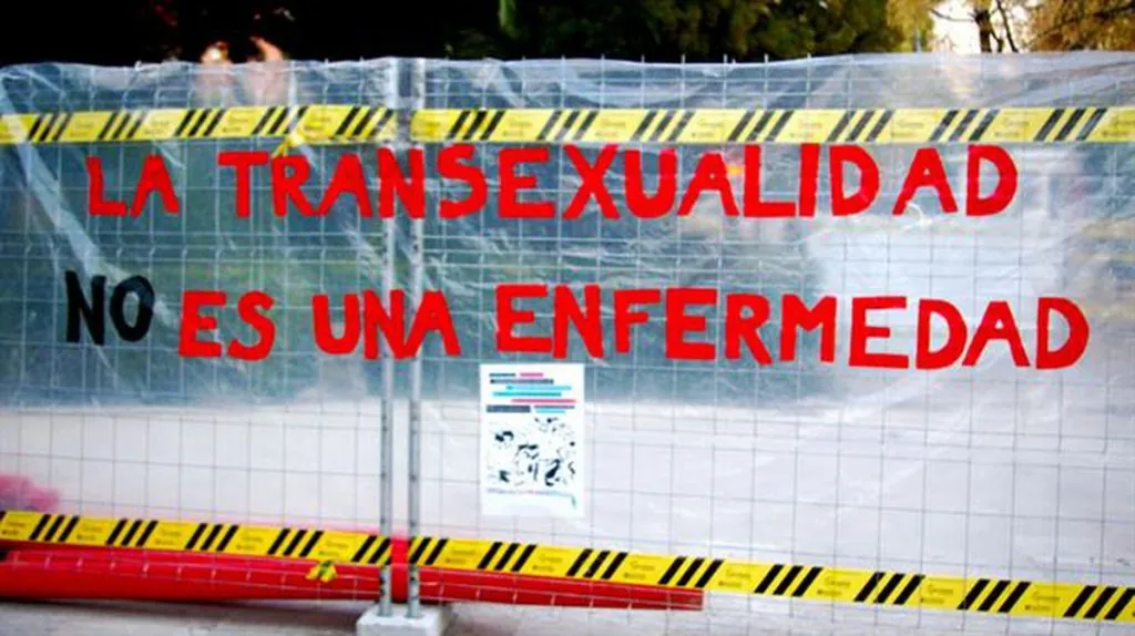 Cartel colgado sobre una reja en el que se lee "la transexualidad NO es una enfermedad"